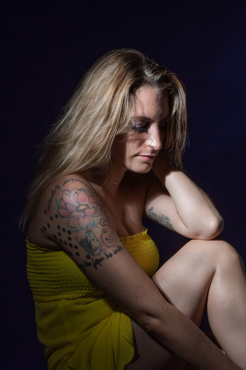 Ragazza in penombra seduta a terra che si accarezza i capelli - Scatto Portfolio