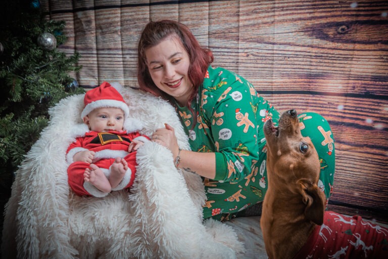 Bimbo newborn vestito da Babbo Natale con mamma e cagnolino che ulula - scatto di Ivan D'Amico Fotografo
